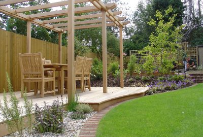 Wooden table under wooden pergola on decking by lawn