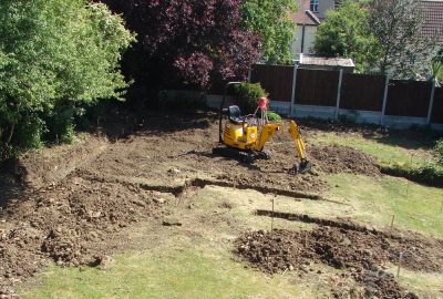 Site clearance with digger digging trenches in lawn